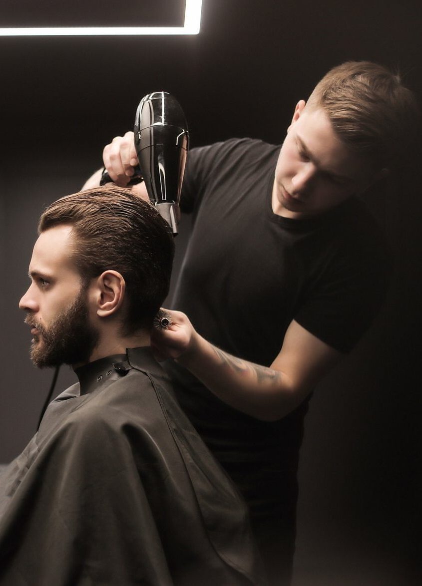 Friseur föhnt die Haare eines Kunden