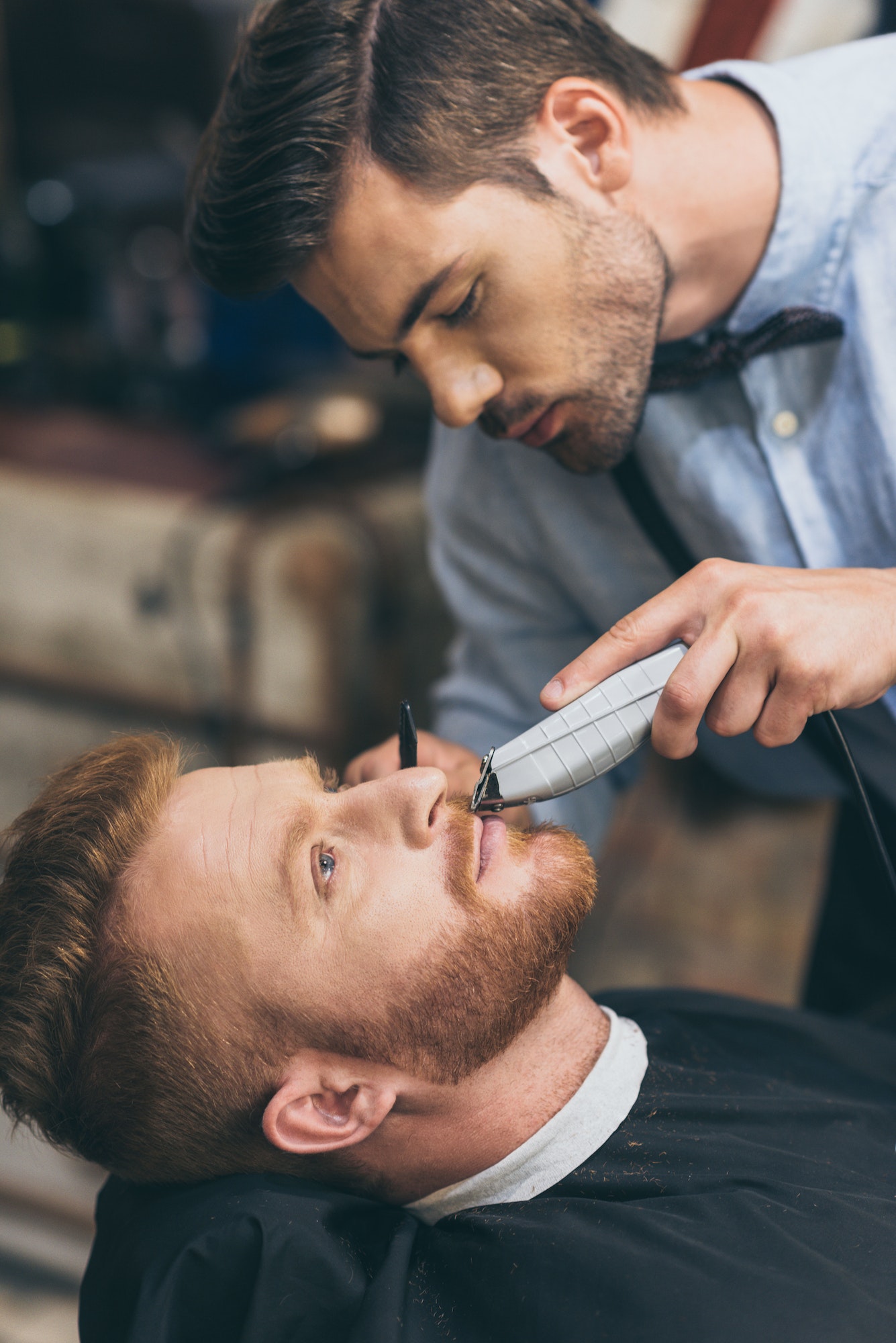 Male barber trimming customers beard in barber shop